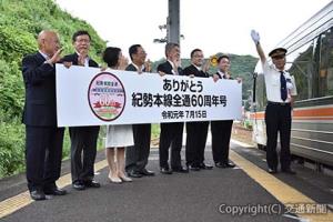 記念列車に合図を送る西尾駅長（右端）、見送る鈴木本部長（右から４番目）ら＝熊野市駅＝