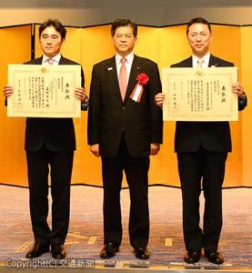 石井大臣（中央）から表彰を受けた伊勢常務執行役員（右）と嘉嶋課長