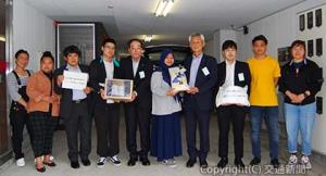 留学生に米を寄贈する末沢社長（右から４人目）、うどん入りの箱を手渡す岡﨑部長（同６人目）ら