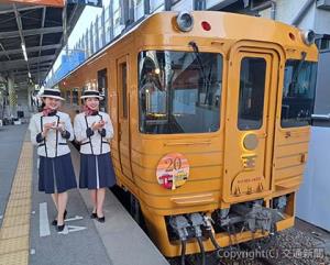 オリジナルデザインのヘッドマークを掲出した列車と缶バッジを持つアテンダント＝松山駅＝（ＪＲ四国提供）