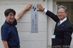 看板を掲げる武藤社長（右）と曽根原所長（ＪＲ東日本リネン提供）